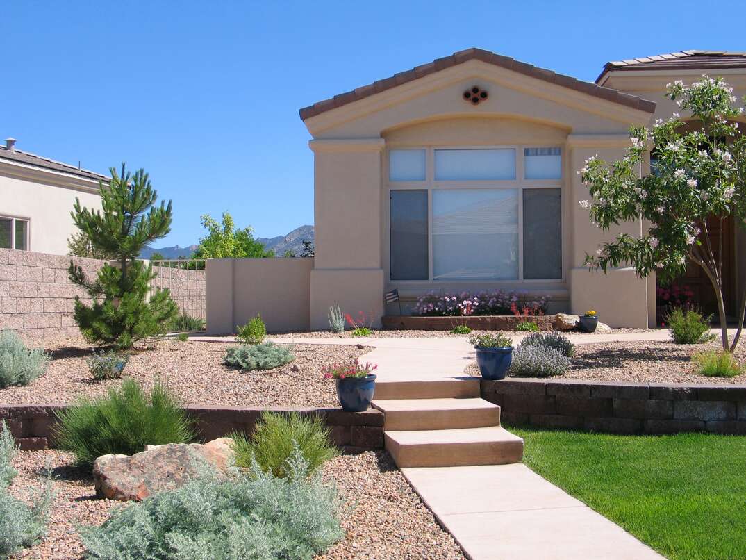 A house in a desert climate is xeriscaped with desert friendly shrubbery and gravel and a small patch of green grass