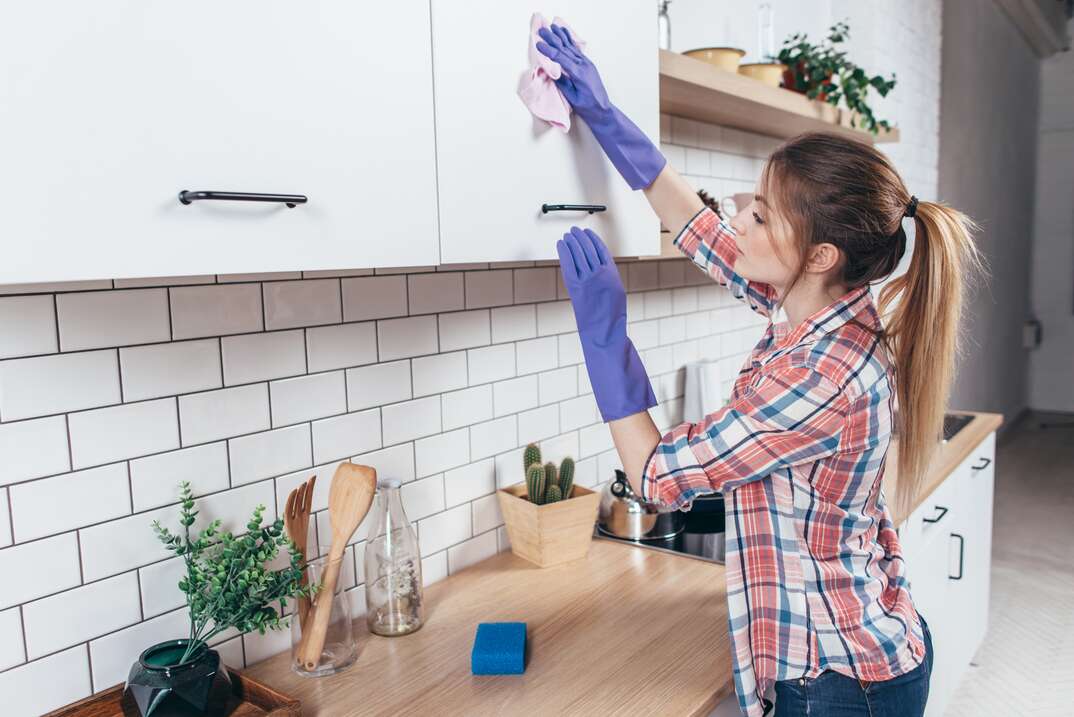 Young woman cleaning the furniture in the kitchen 