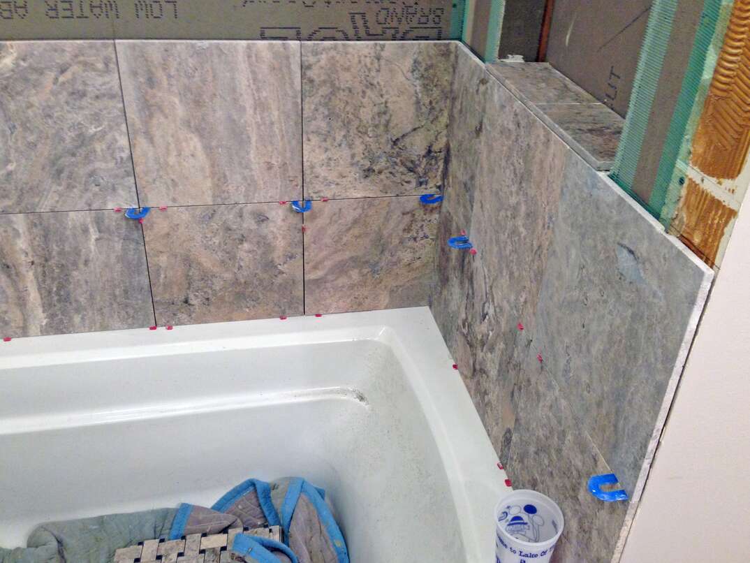 bathtub with travertine stone tile being installed