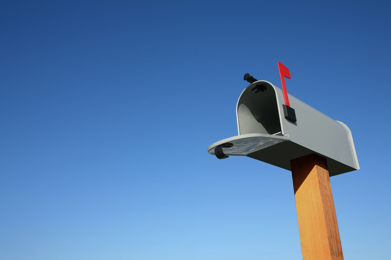 A gray mailbox sits with its red flag up and door open atop a brown wooden post against the backdrop of a cloudless blue sky, mailbox, gray mailbox, red mailbox flag, mailbox flag, flag up, brown wooden post, wooden post, blue sky, sky, blue