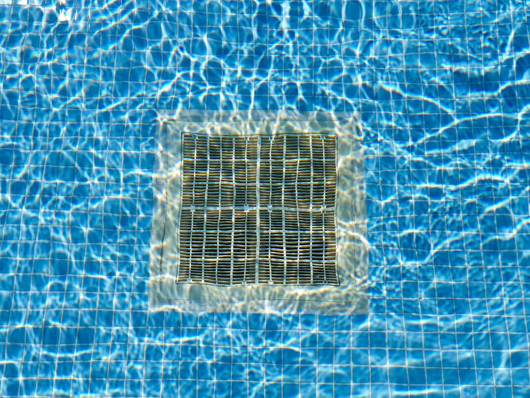 Pulsating blue pool water with reflections of the sun Drain grate for water at the bottom of the pool