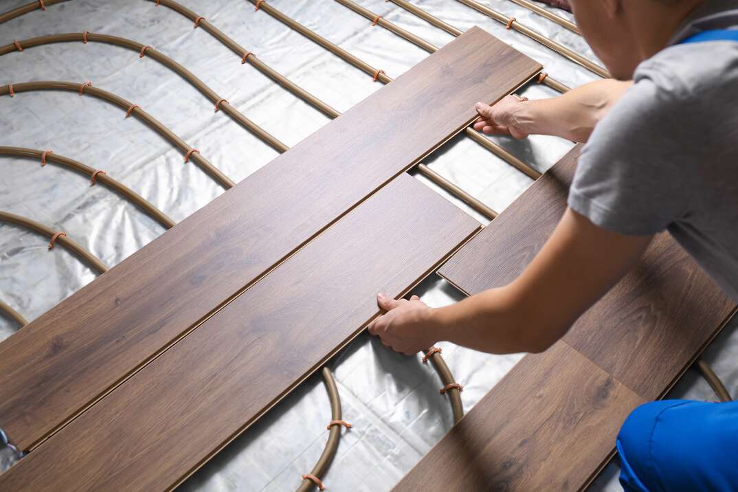 Worker installing new wooden laminate over underfloor heating system shown in closeup, wood slats, woodgrain, brown wood flooring planks, wood flooring planks, flooring planks, flooring, planks, hardwood floors, hardwood flooring, hardwood, flooring, radiant flooring, radiant, radiant heat, heat, heated floors, heated flooring, hvac, heating, electrical, electric, electricity, HVAC, installation, install, flooring installer, floor installer, underfloor, subfloor