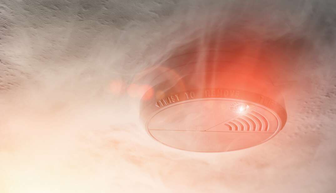 A smoke detector with smoke and red warning light in a apartment roof. ideal for websites and magazines layouts.