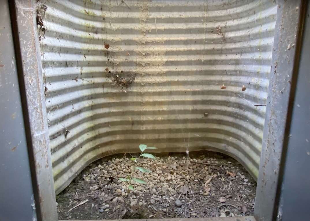 Landscaping gravel sits at the base of a corrugated steel window well of a basement egress window