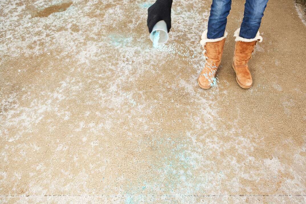 A woman is spreading blue rock salt on a frozen winter driveway 