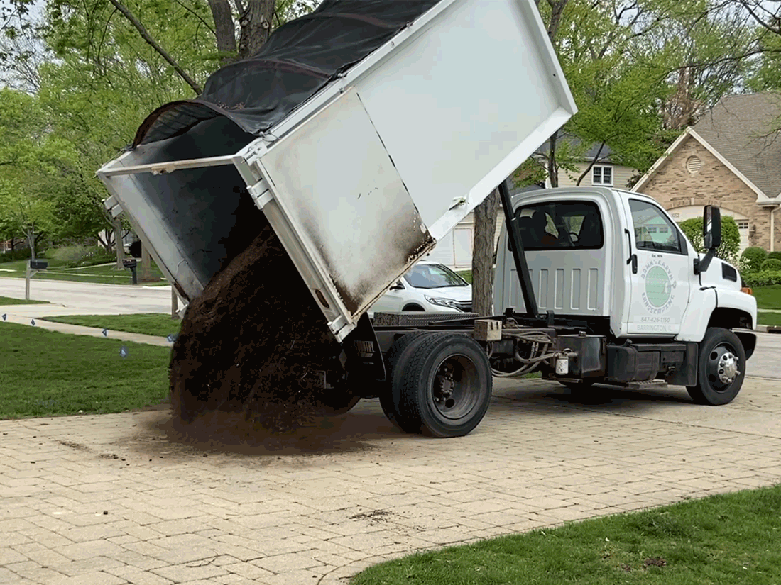 Animated visual of a dump truck delivering hardwood mulch on a residential driveway