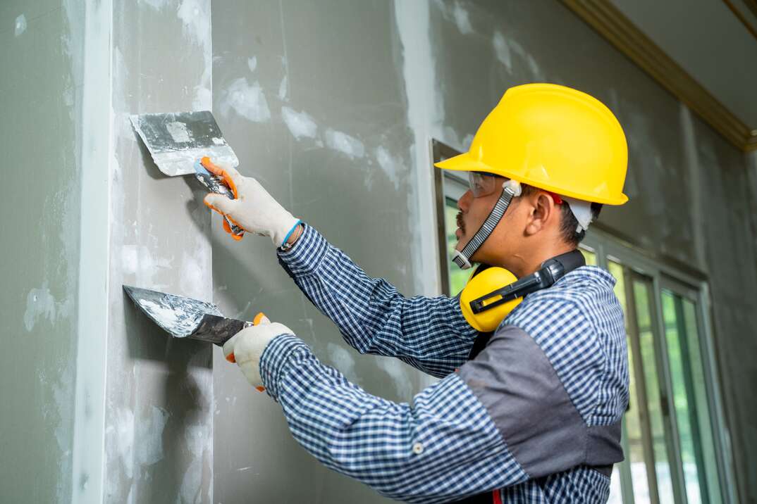 Construction industry worker using a putty knife and leveling in house under reconstruction 