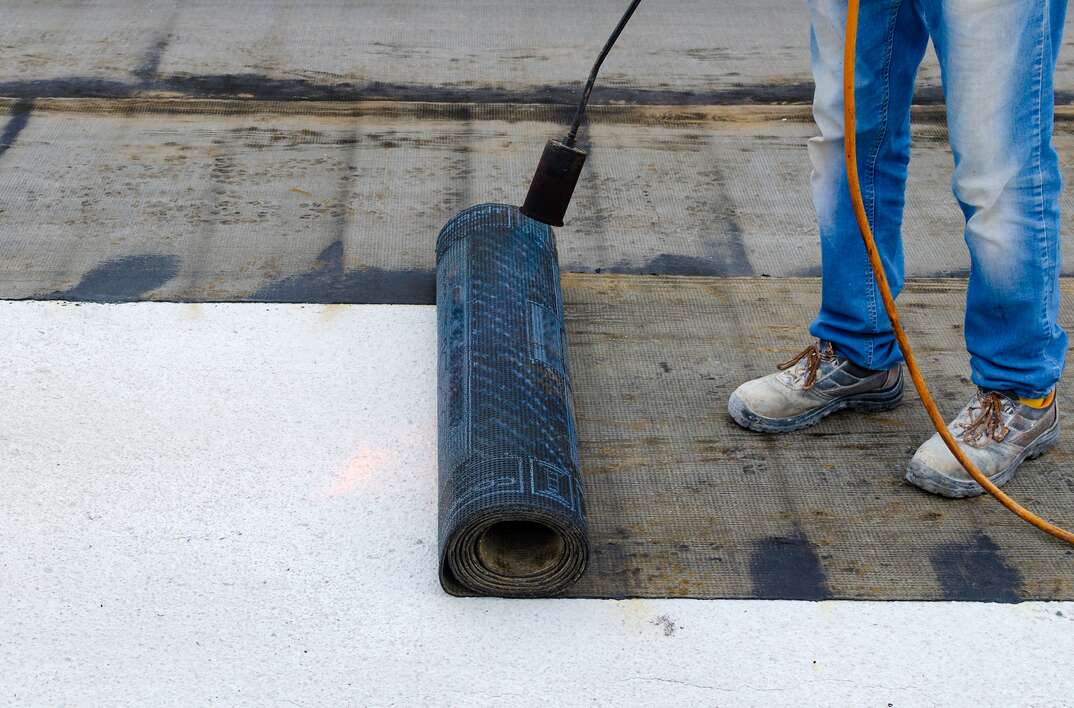 Roofer installing rolls of bituminous waterproofing membrane for the waterproofing of a terrace