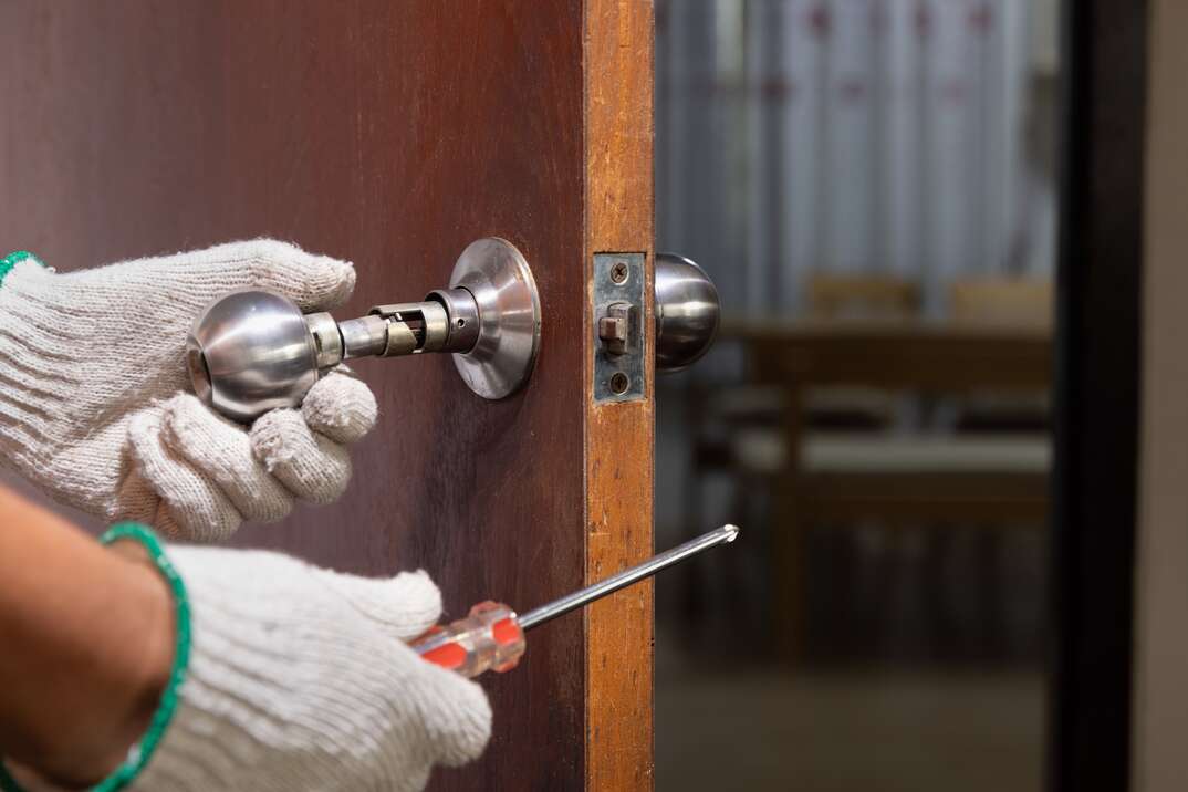 Locksmith on wood door with screwdriver for repair or fix silver knob.