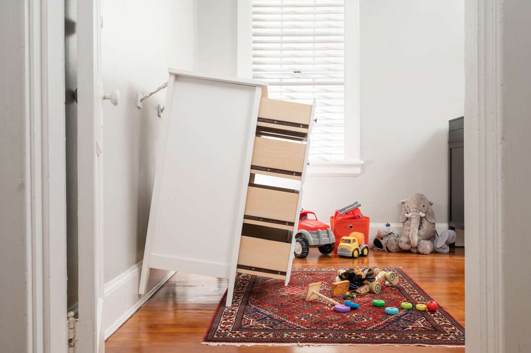 A white dresser leans away from the wall in a children s bedroom