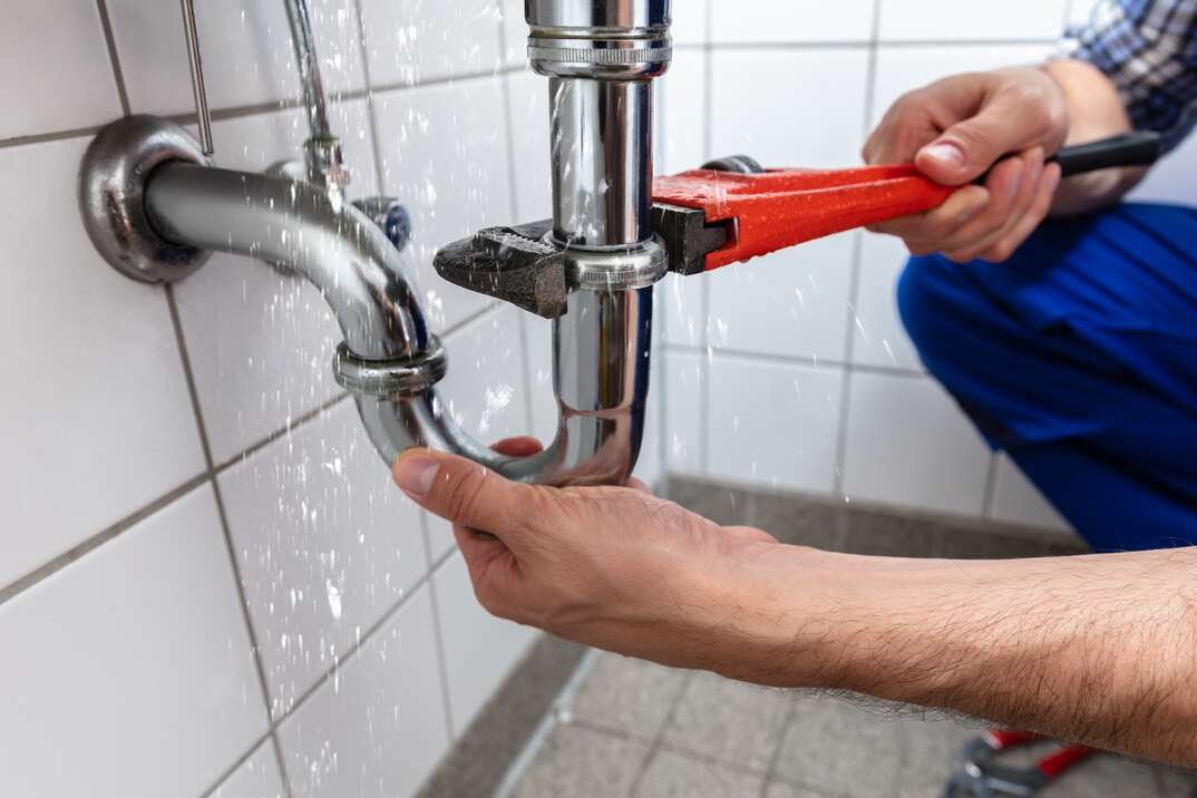 male plumber s hands repairing a leaking sink pipe with a adjustable wrench