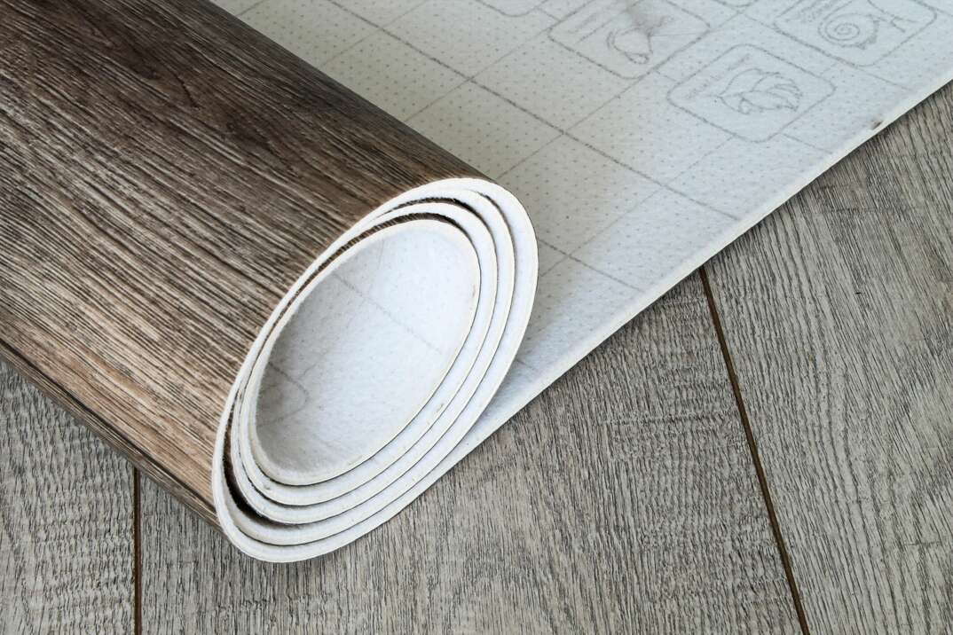 A roll of simulated wood vinyl tile is unrolled across a finished floor 