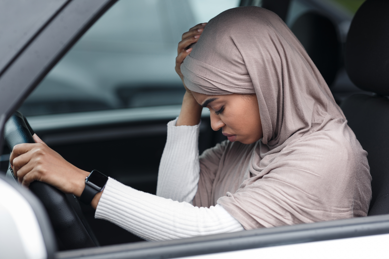 Accident in city, traffic problems, feeling unwell and injury in car. Despair millennial islamic african american lady driver in hijab on steering wheel presses hand to head suffering from headache
