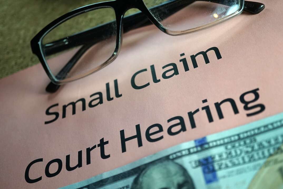 A pair of eyeglasses sits atop a piece of paper with the words Small Claim Court Hearing printed on it and a one hundred dollar bill sitting beneath the words, eyeglasses, glasses, small claim court hearing, small claim court, court, courtroom, court case, legal, small claims court, money, hundred dollar bill, cash, bill