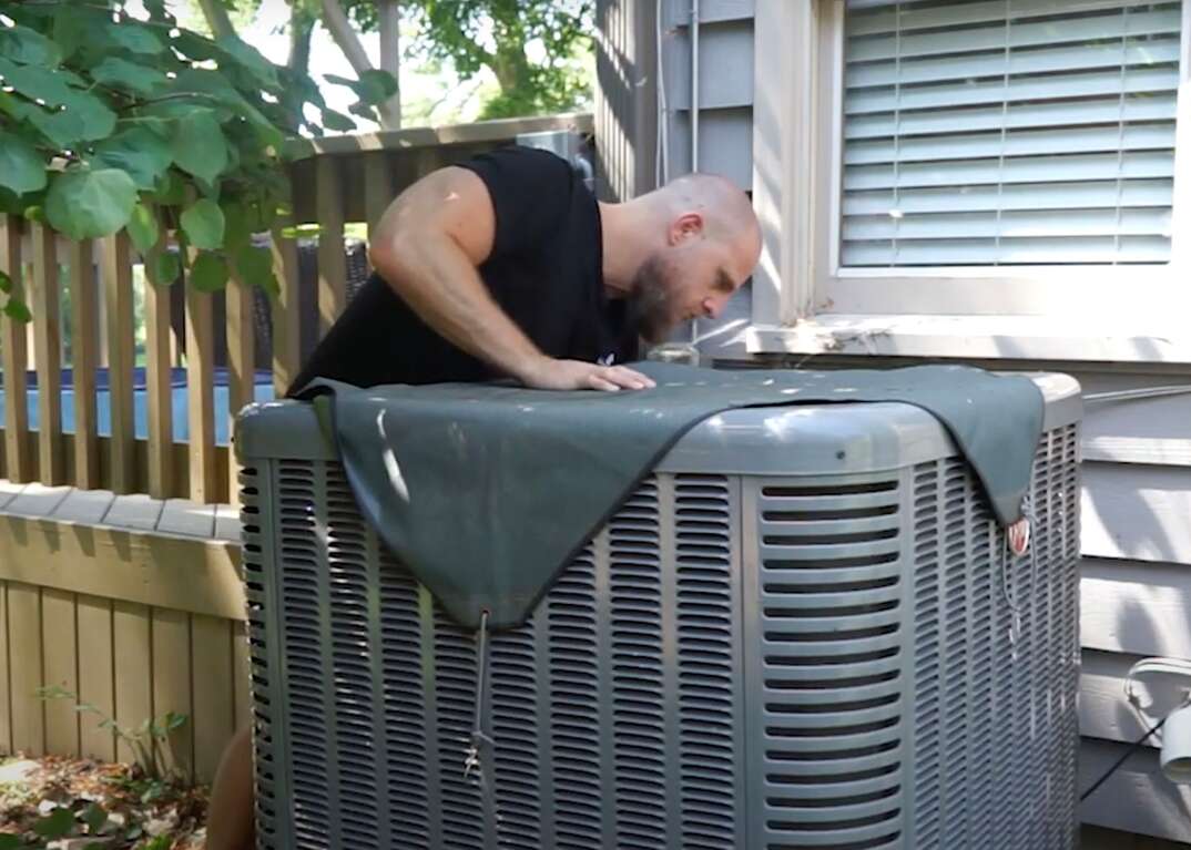 Man puts cover on AC unit outside a home near a wooden deck in the backyard.