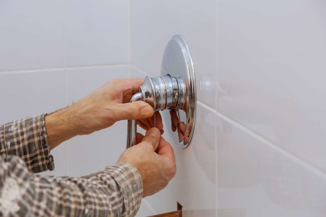 Plumber hands fixing shower mixer on modern water tap 