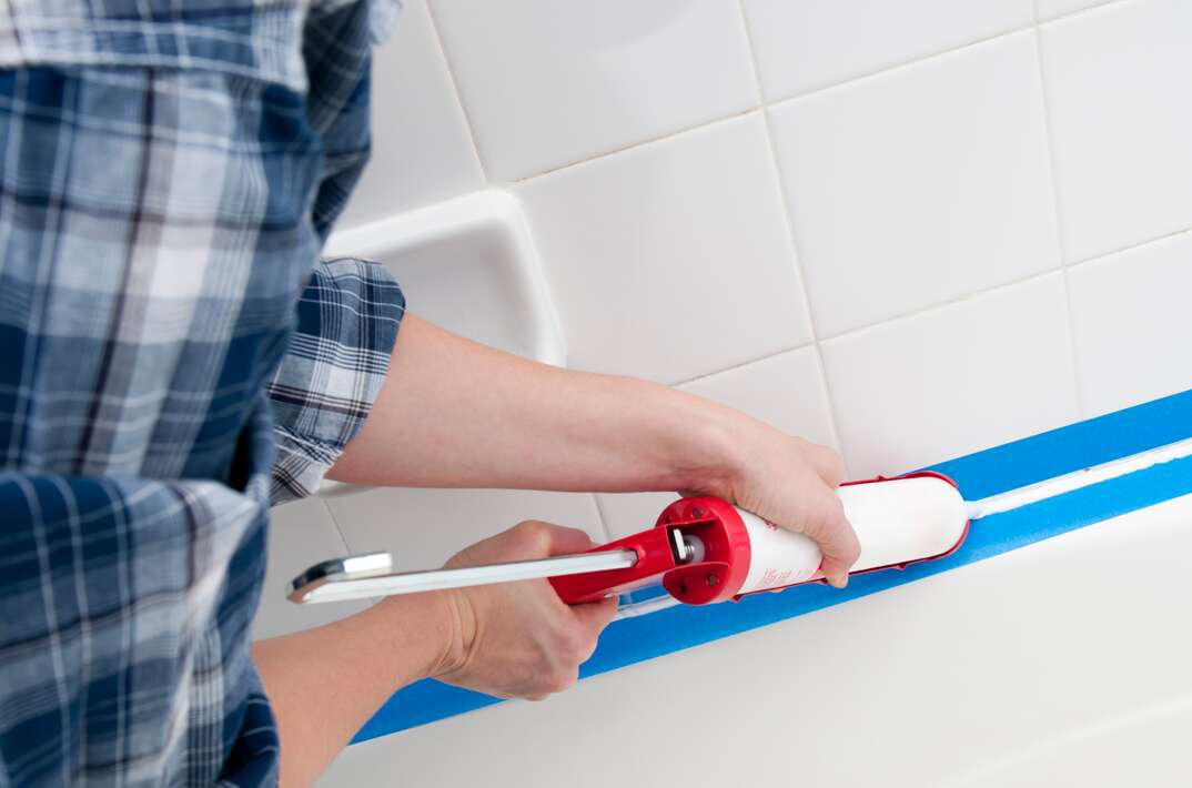Applying caulk to a bathtub with blue painter s tape