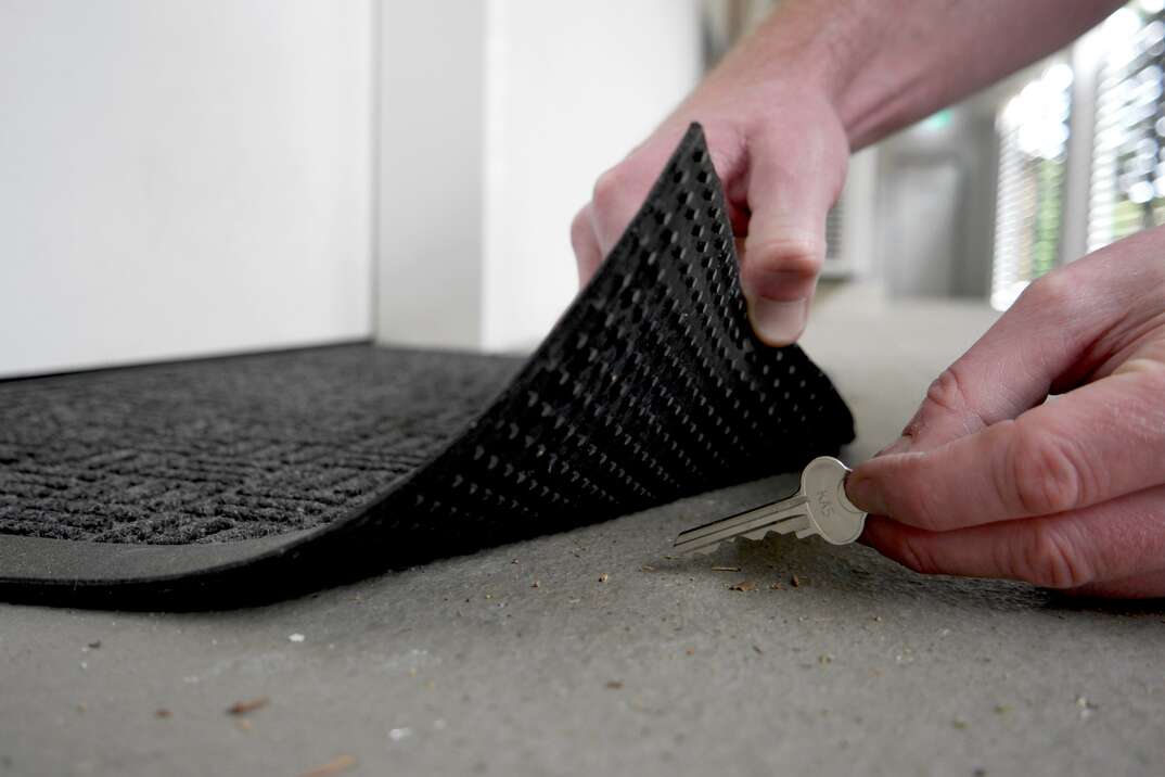 Man lifting edge of a door mat to pick up a key hidden underneath