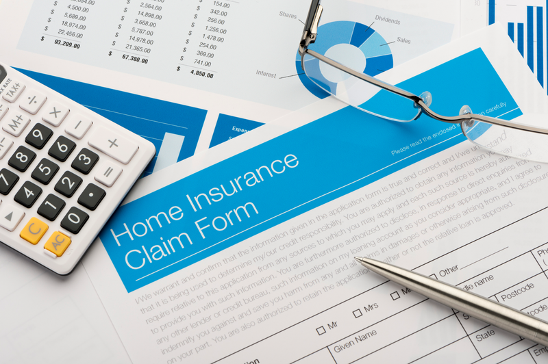 A home insurance claim form sits on a desktop along with a pen and a calculator and a pair of eyeglasses, eyeglasses, glasses, calculator, form, document, home insurance form, homeowners insurance, renters insurance, claim form, insurance claim, pen