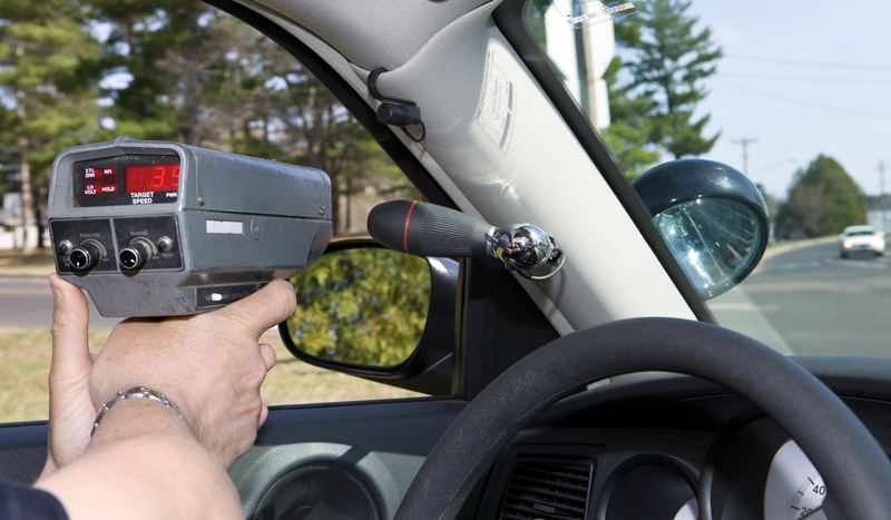 A police officer in a patrol car points a speed detector gun out the window in an attempt to catch speeding drivers, police officer, officer, cop, police, radar gun, speed detection gun, speed detection, law enforcement, traffic, traffic cop, police car, patrol car, speeding, speeding ticket, speed trap