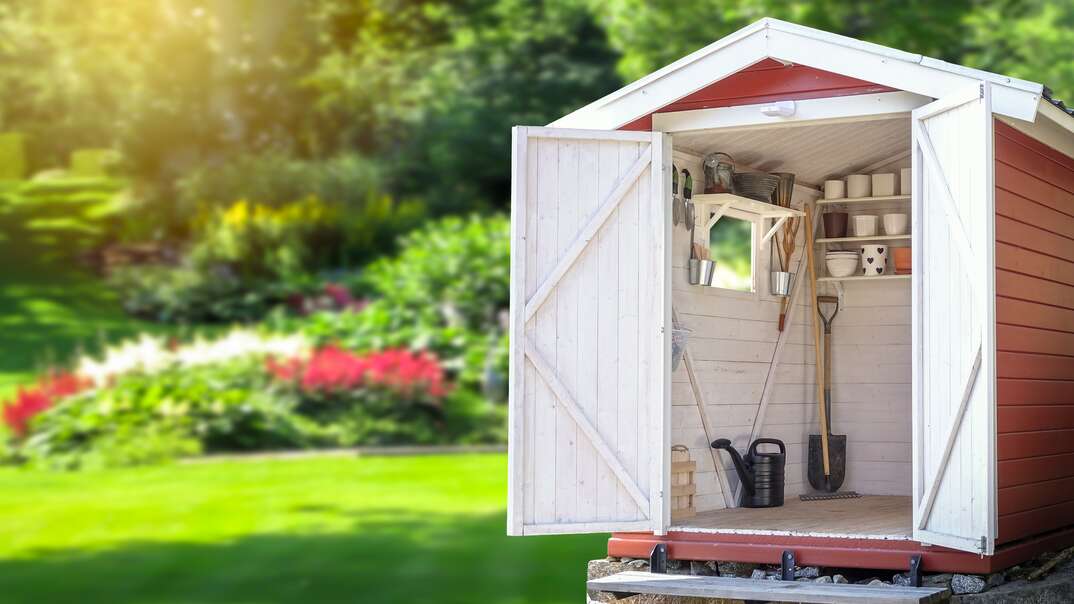 Storage shed filled with gardening tools  Beautiful green botanical garden in the background 