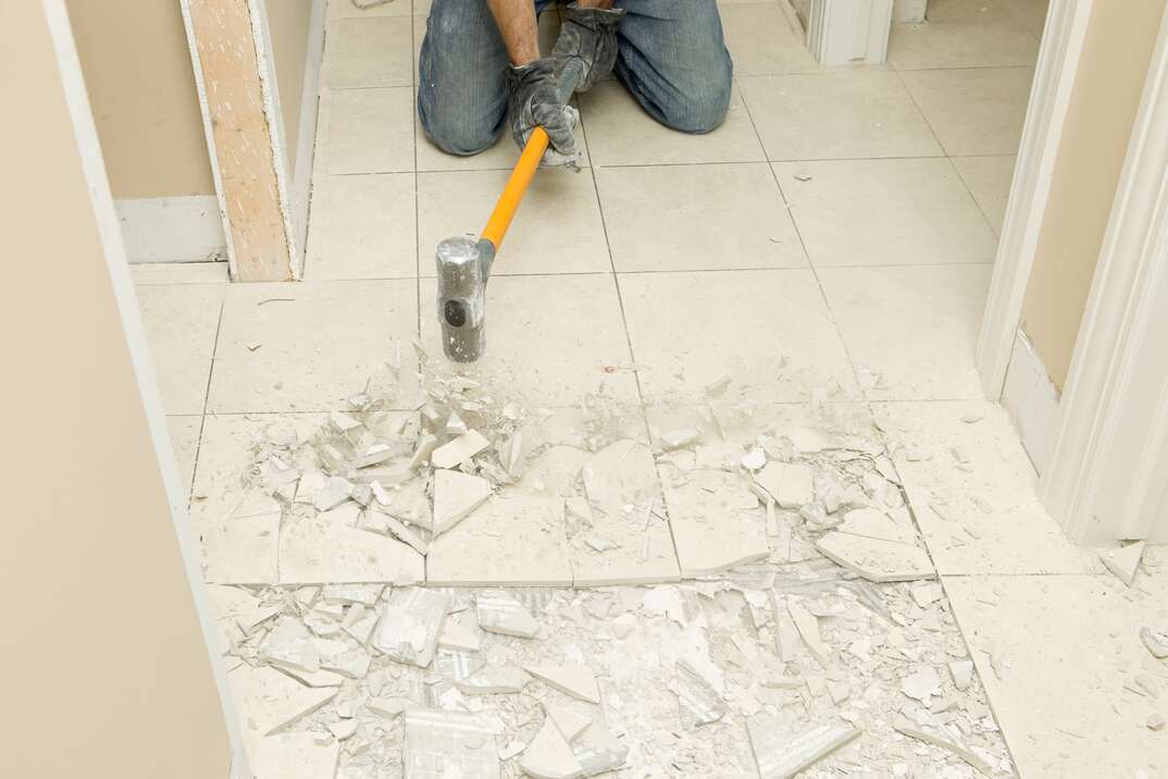 Construction Worker Demolishing Hallway Tile with Sledgehammer