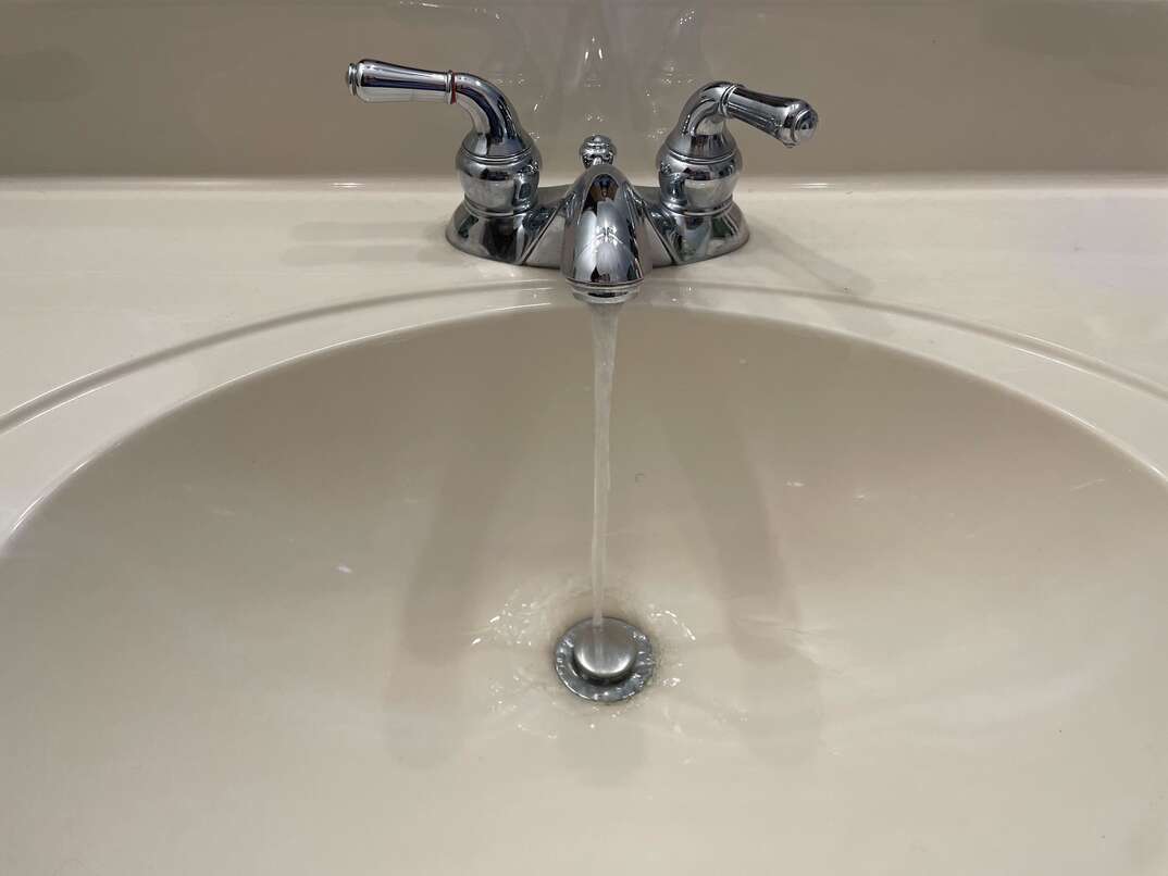 white bathroom sink with metal faucet and stopper drain and running water