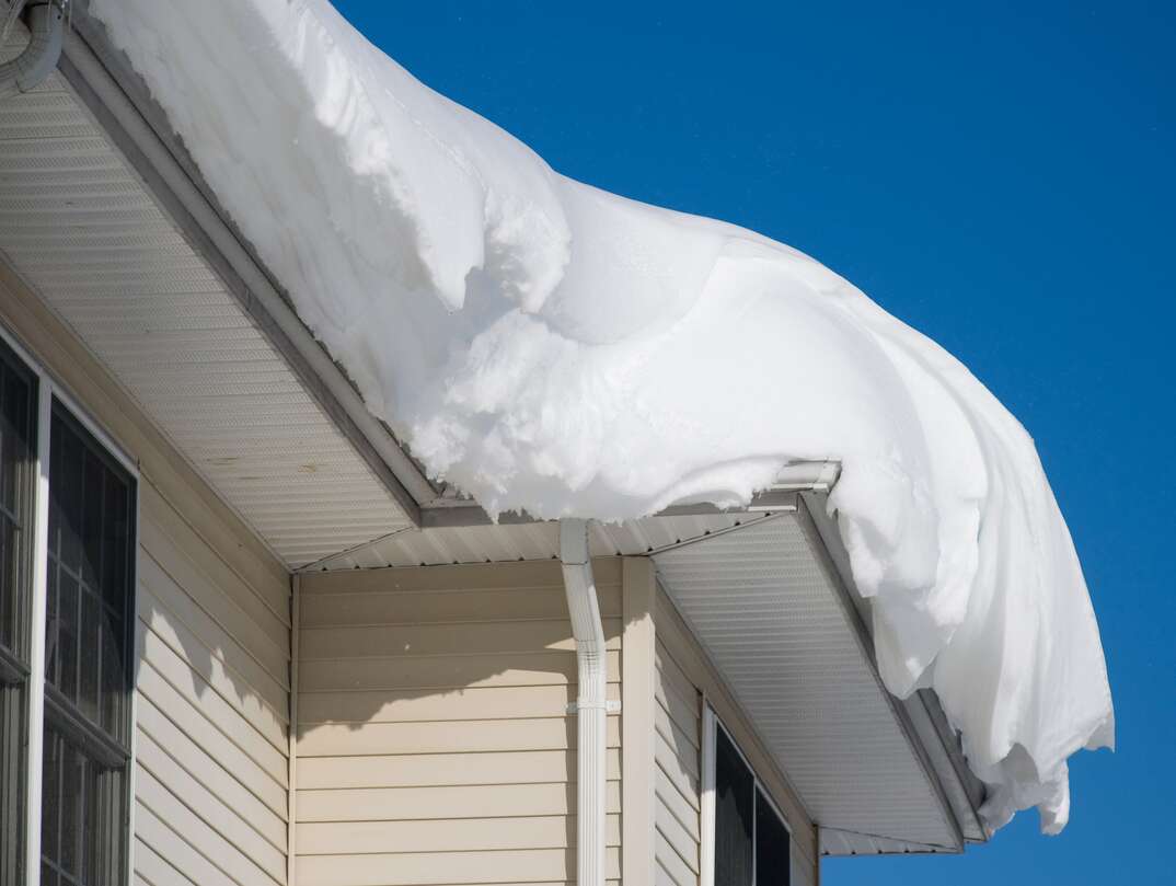 a beige residential home covered with a massive amount of snow on a clear day 