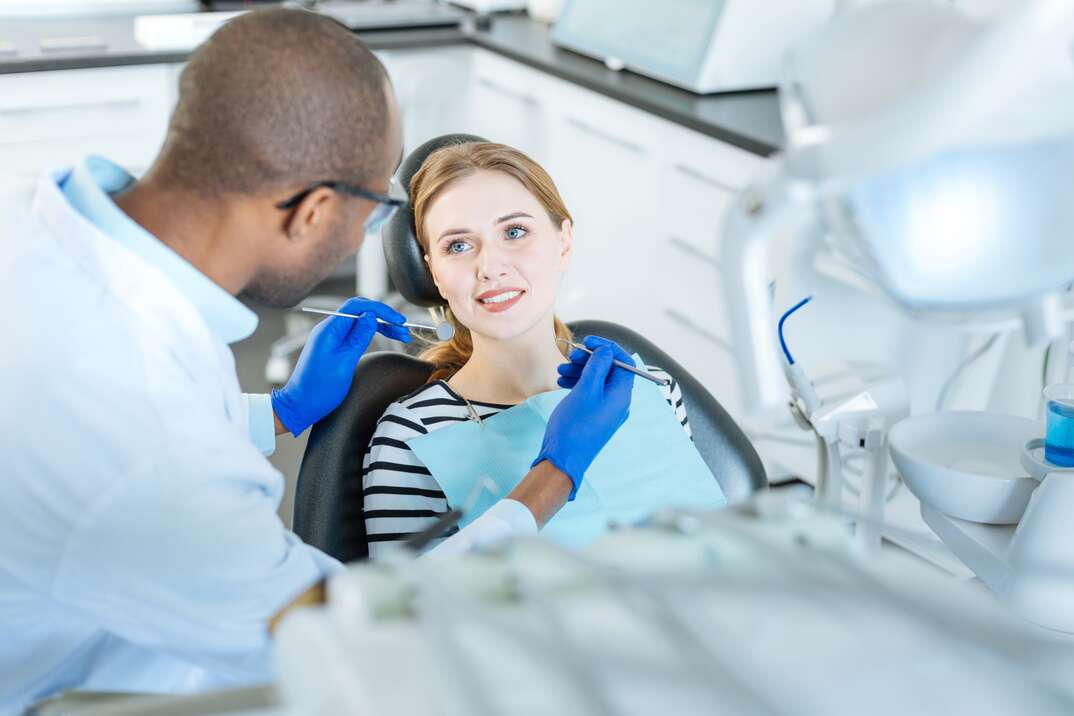 Look of gratitude. Beautiful young woman sitting in a dentist chair and smiling at her dentist while he holding a mouth mirror and a probe for a checkup