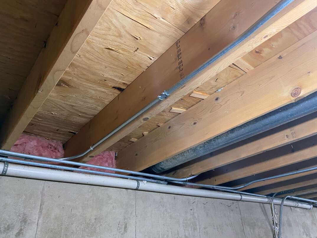 photo taken in a residential basement looking up at floor joists from the first level 