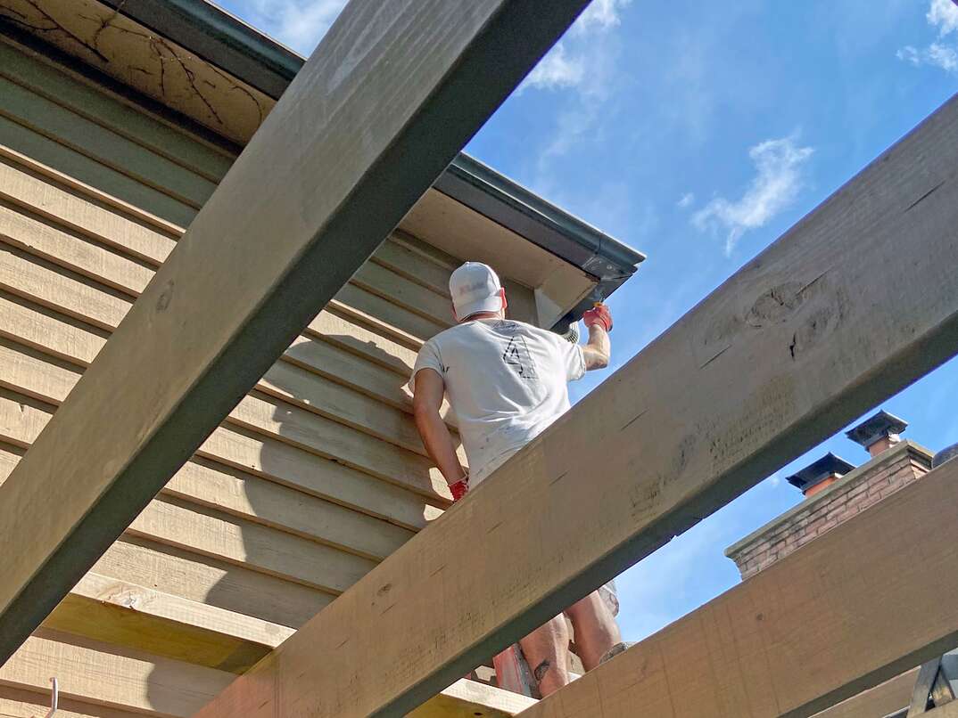 man standing on pergola painting a house
