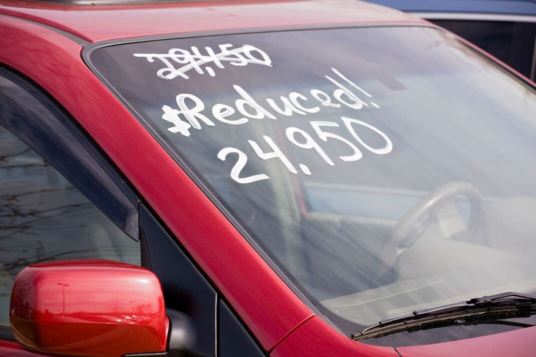 A red vehicle with writing on the windshield indicates that the price has been reduced significantly, red car, car, used car, vehicle, used vehicle, writing, price, pricing, reduced price, windshield, reduced, dealership, car dealership, used car dealership