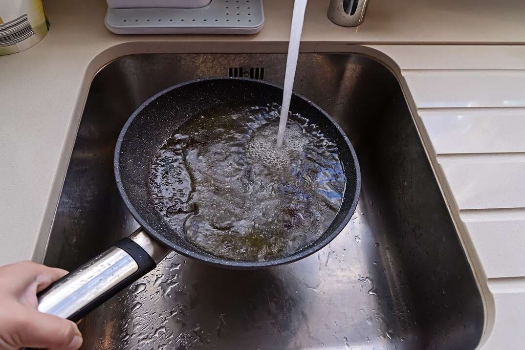 Frying pan with non-stick surface and hot oil under water tap flow in sink