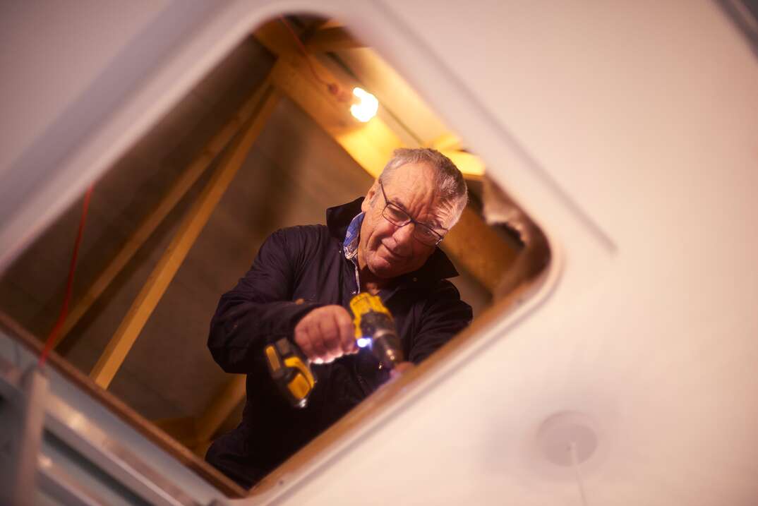 man works to secure screws into a pull-down attic ladder