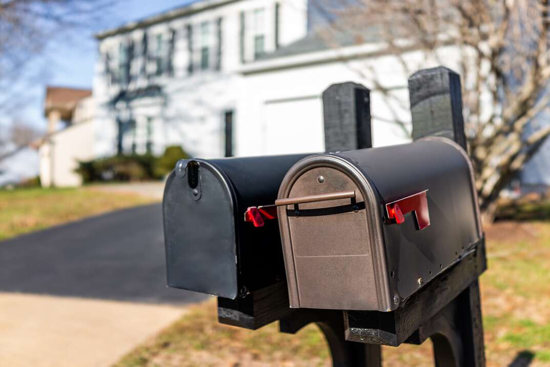 Closeup of two modern black and brown metal red flag mailboxes at single family home in residential suburbs with nobody and house in background