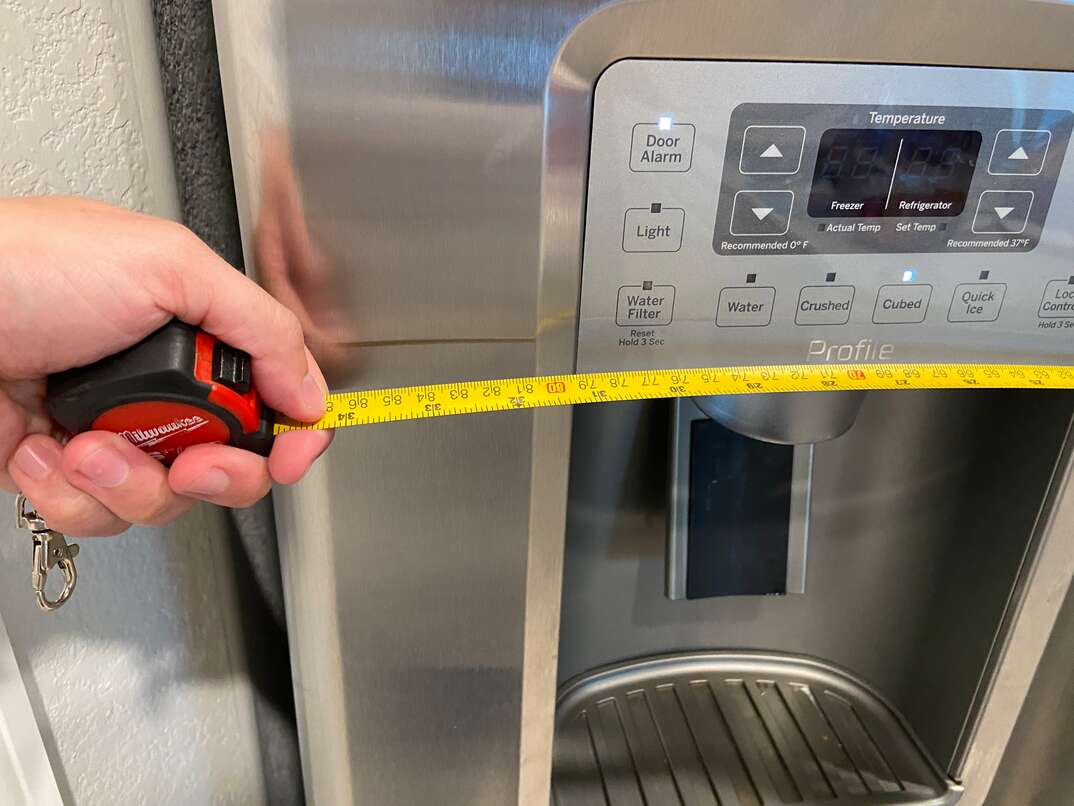 Male holds a pocket rules to measure the width of a stainless steel refrigerator 
