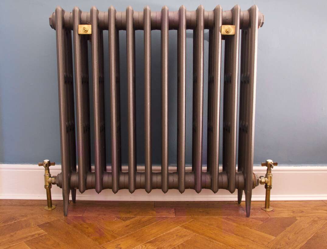 Old fashioned cast iron radiator with brass fittings on herringbone wooden floor. High quality photo