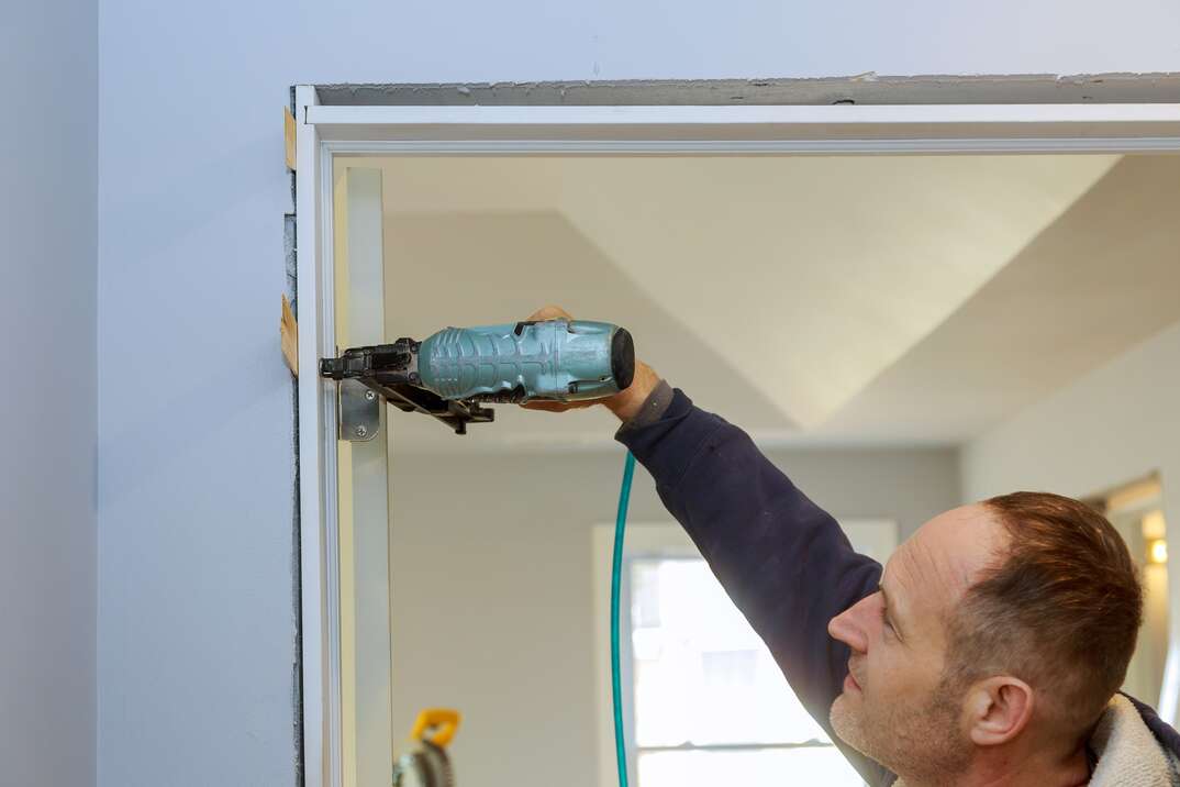 Contractor using pnumatic nail gun installing the interior door of apartment