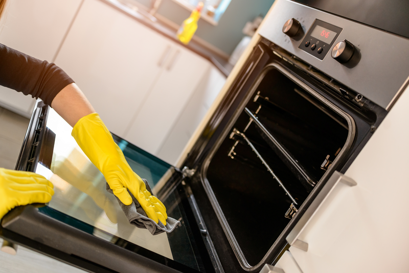 Closeup on woman's hands in yellow protective rubber gloves cleaning oven with rag