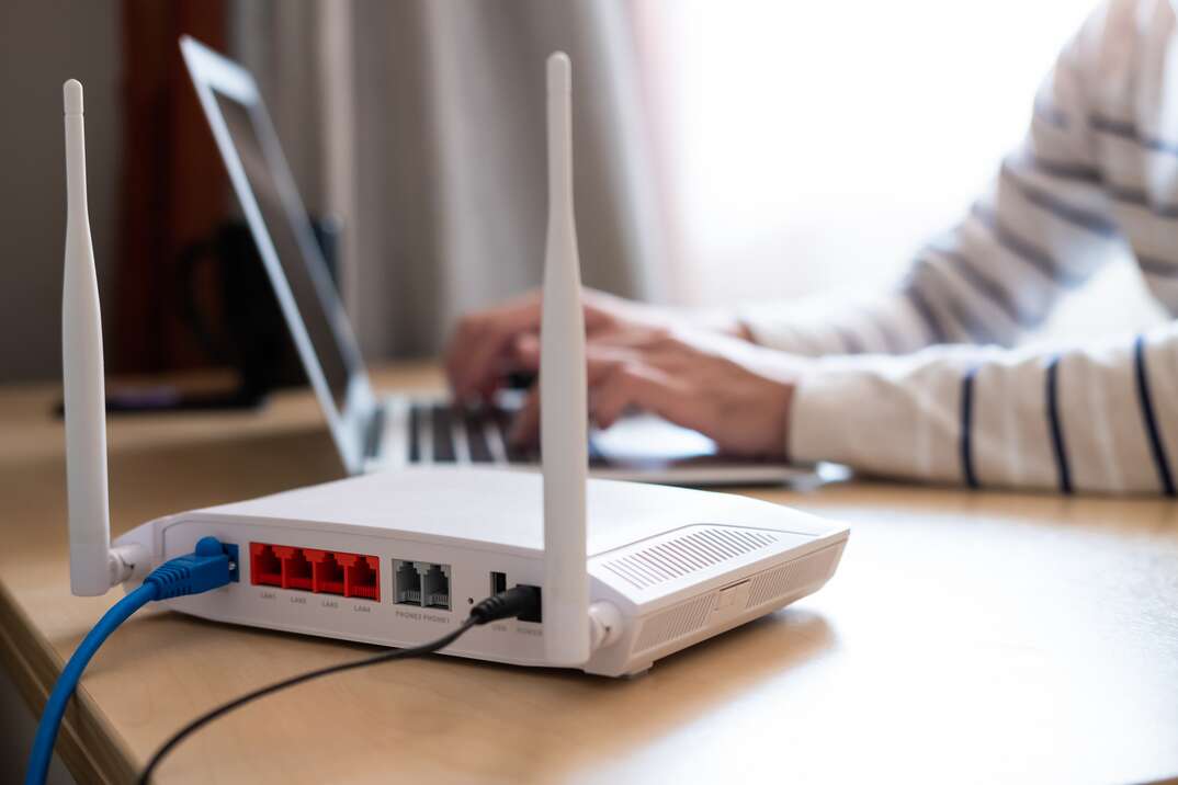 Selective focus at router  Internet router on working table with blurred man connect the cable at the background  Fast and high speed internet connection from fiber line with LAN cable connection 