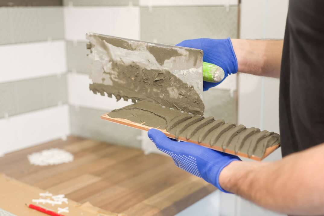 hands of tile installing ceramic tiles on a kitchen backsplash