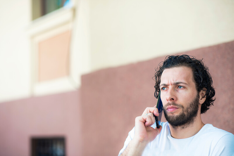 Worrying phone call, young bearded man expressing worry while talking on his cell phone, outdoor urban scenery
