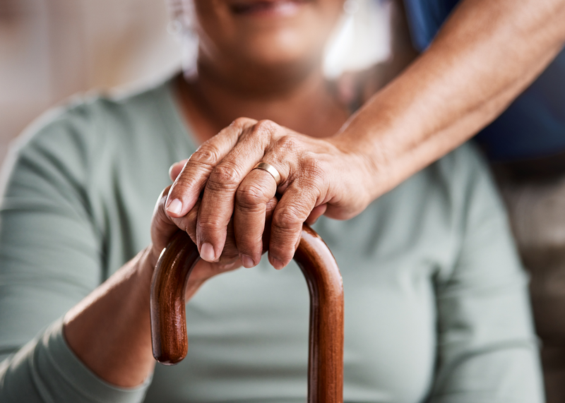 An elderly woman holds a walking cane as the hand of a male wearing a wedding ring places his hand on top of hers, married, wedding ring, ring, human hand, human arm, woman, elderly woman, woman holding cane, cane, walking cane, older woman, older