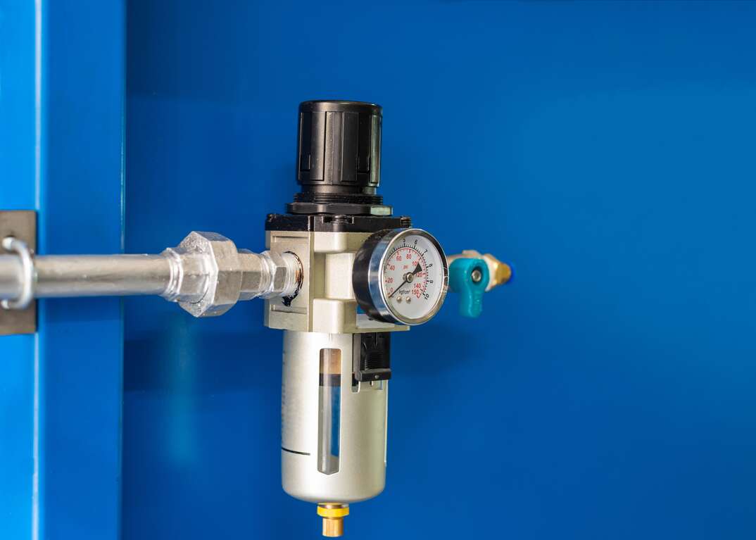 A water pressure regulator device with a gauge is shown against a blue background, water pressure regulator, regulator, gauge, blue background, blue, water pressure, water, pressure, plumbing, plumber