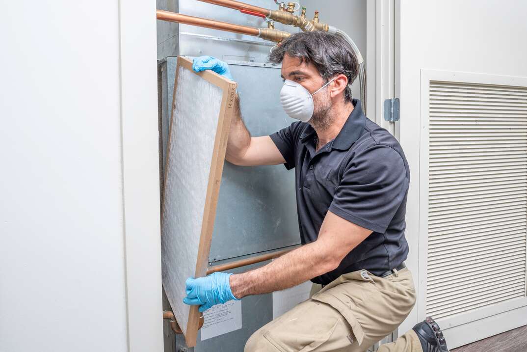 HVAC tech wearing mask and gloves changing an air filter