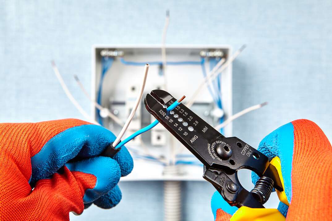 electrician using stripper cutter tool to strip the end of the electrical wire when repairing and updating wiring in the home grid