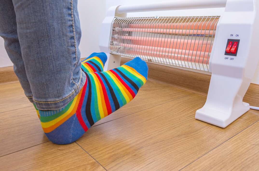 A person wearing bright rainbow-colored socks and warms cold feet near an electric heater. Infrared halogen heater at home.