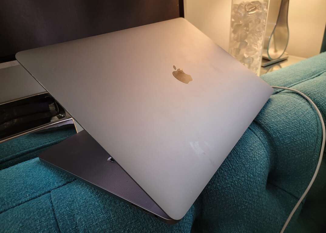 An An Apple brand MacBook laptop computer sits  on the back of a couch in a room
