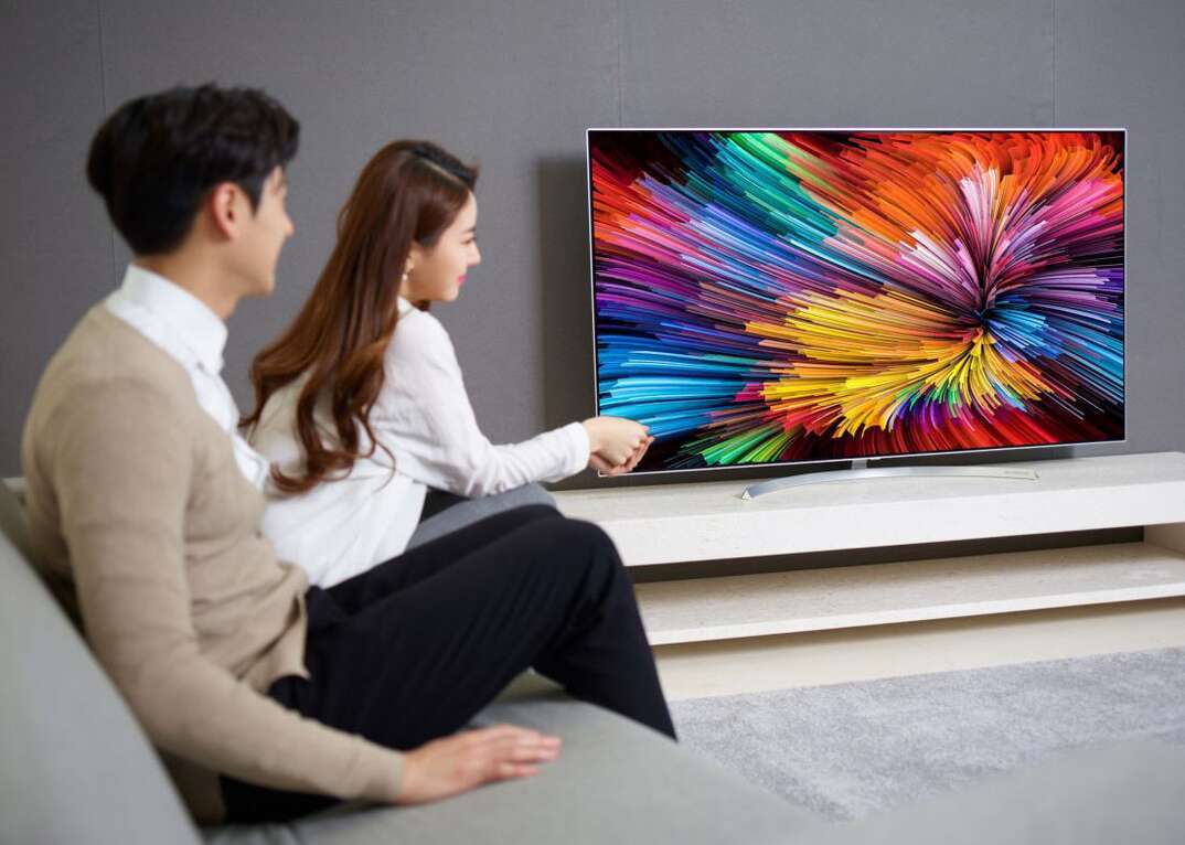 A couple sit on the couch in their living room in front of an LG brand flatscreen TV with a colorful pattern on the large screen