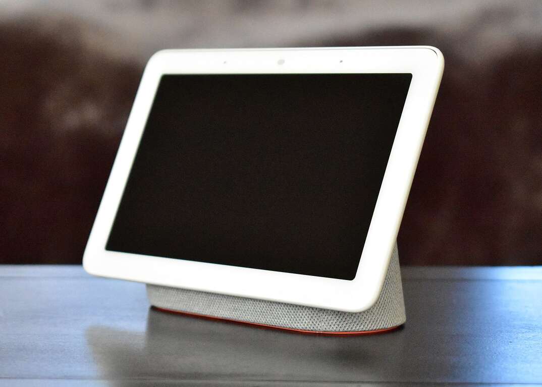 A white Google Nest Home device with blank, black screen rests on a table.